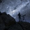 A silhouette of a person with a telescope against a dark, starry sky.